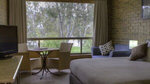 A hotel room with a bed, a desk, a chair, a small table, and a sofa. There is a window with a view of trees. - Mannum Motel (Mannum)