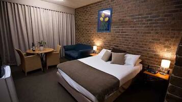 A hotel room with a large bed, a desk, a chair, and a small table.