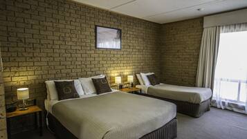 A hotel room with two beds, a brick wall, a framed picture, and a window with curtains.