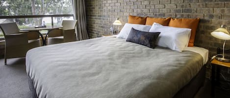 A hotel room with a large bed, two bedside tables, a window with a view of trees, and a brick wall.