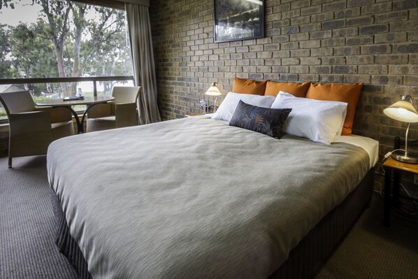A hotel room with a large bed, two bedside tables, a window with a view of trees, and a brick wall.