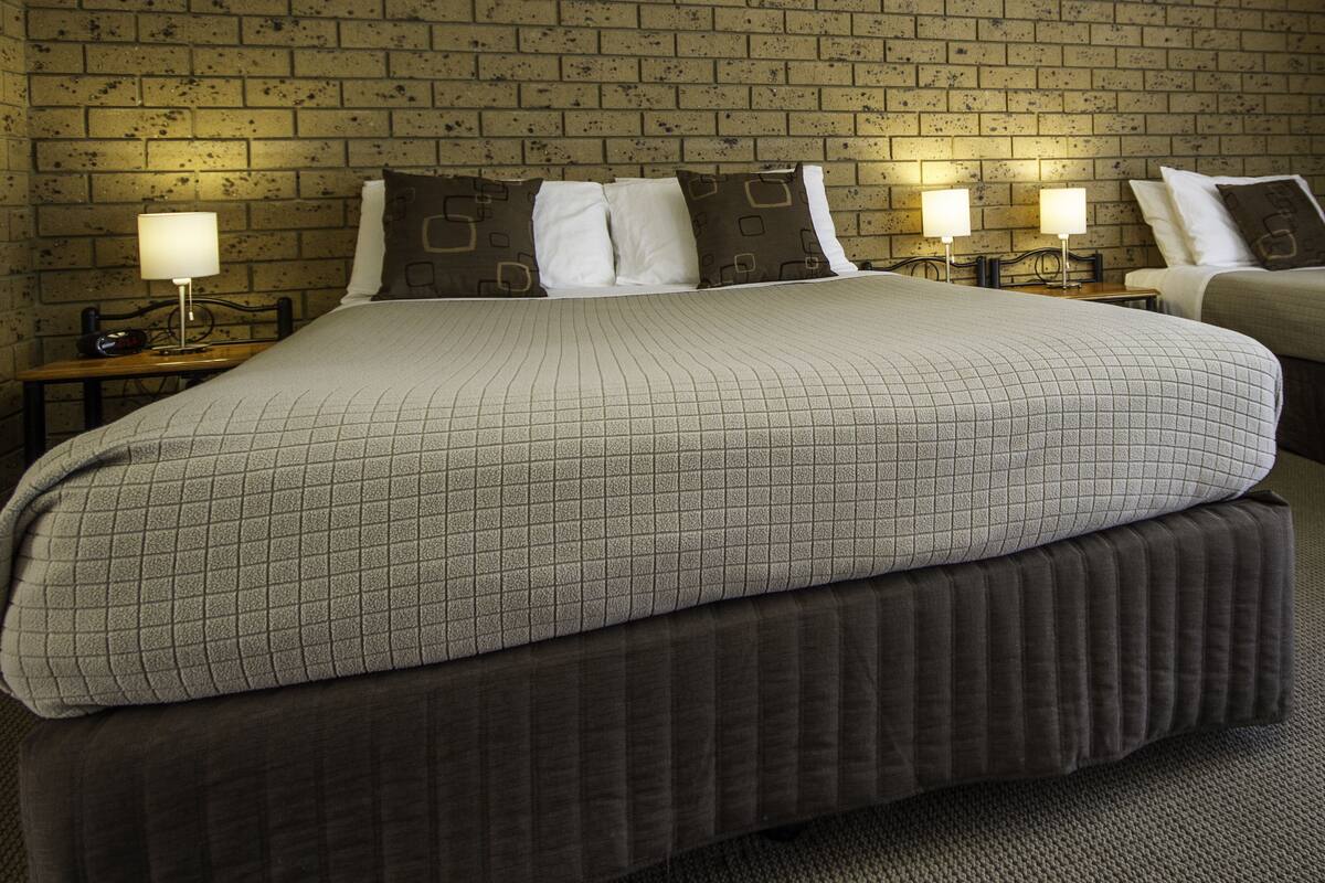 A hotel room with a large bed, two bedside tables with lamps, and a brick-patterned wall.