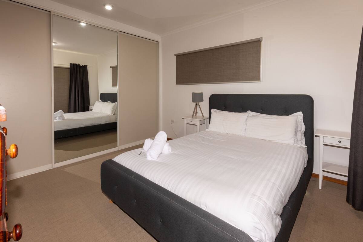 A modern hotel room with a large bed, a bedside table, a lamp, and a mirror.