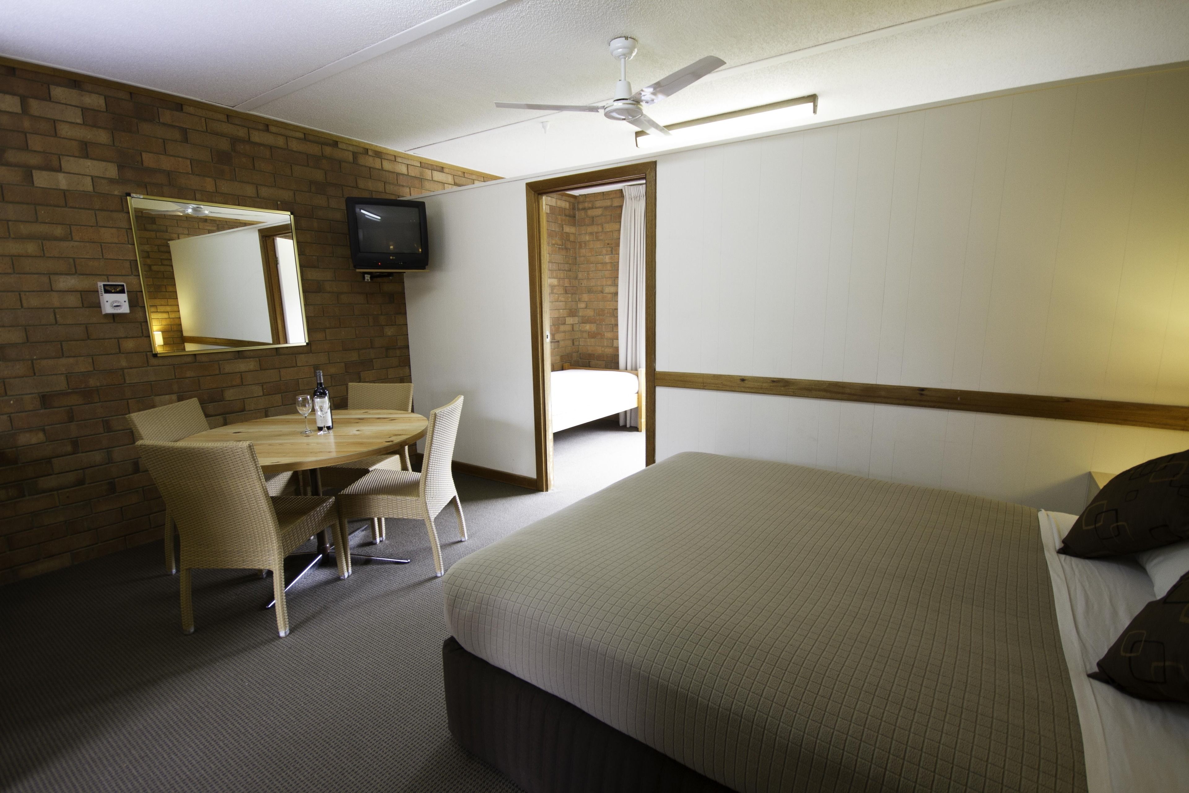 A hotel room with a bed, a desk with a chair, a television, and a ceiling fan.