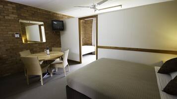 A hotel room with a bed, a desk with a chair, a television, and a ceiling fan.