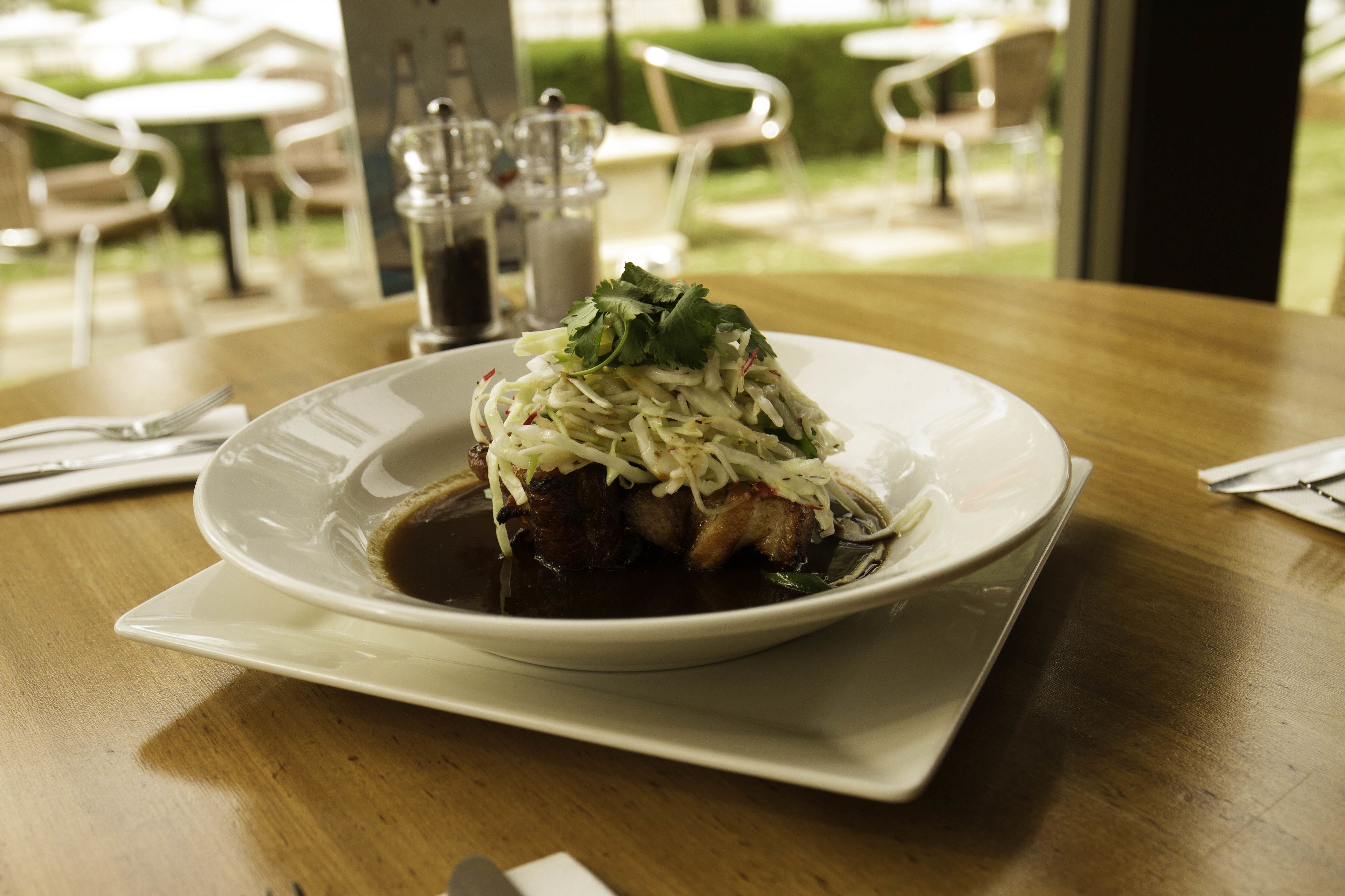 Un plato de comida con salsa oscura, adornado con hojas verdes, sobre un plato blanco.