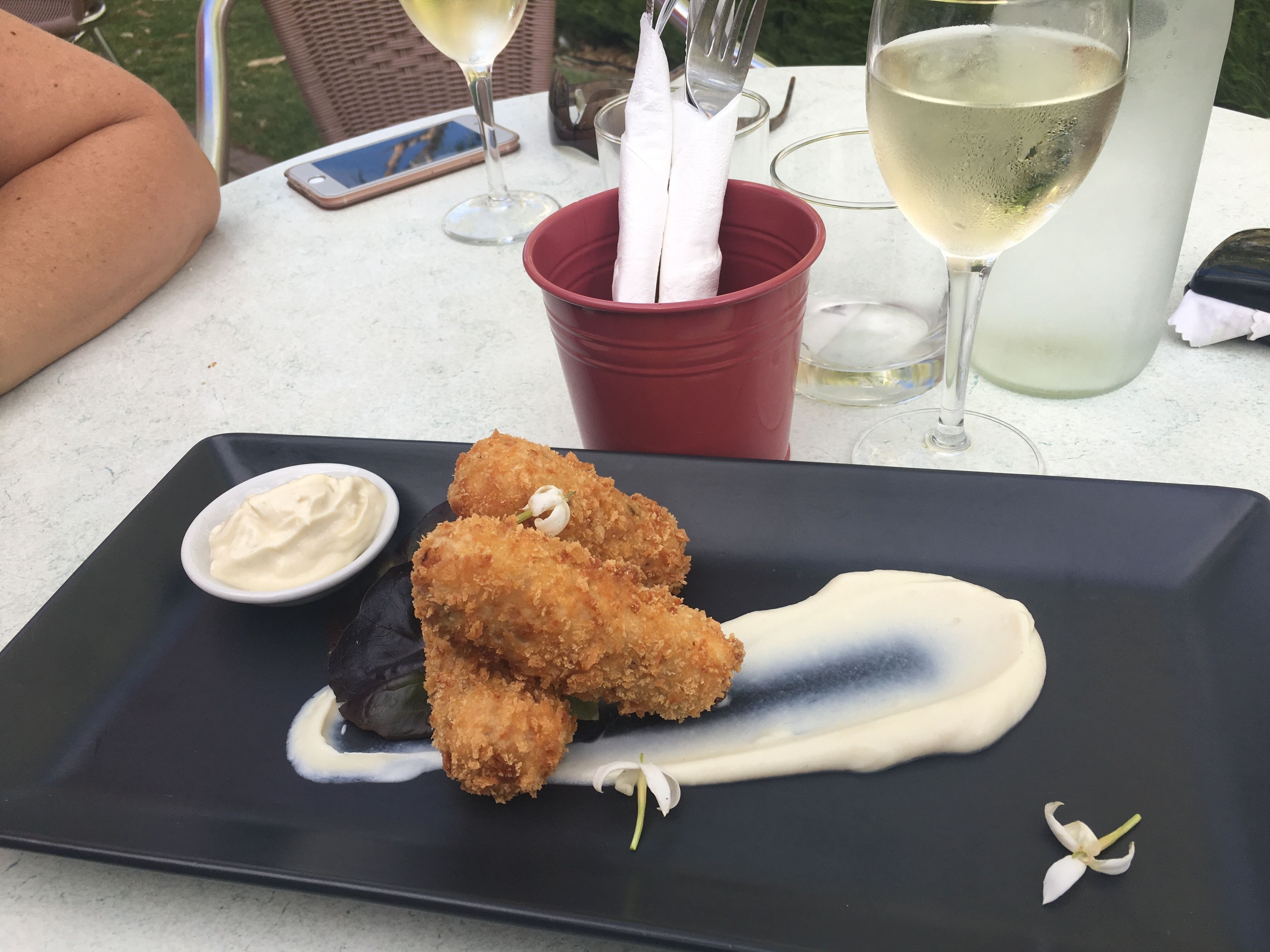Una mesa de comedor con un plato negro de comida frita, una taza roja y dos copas de vino blanco.