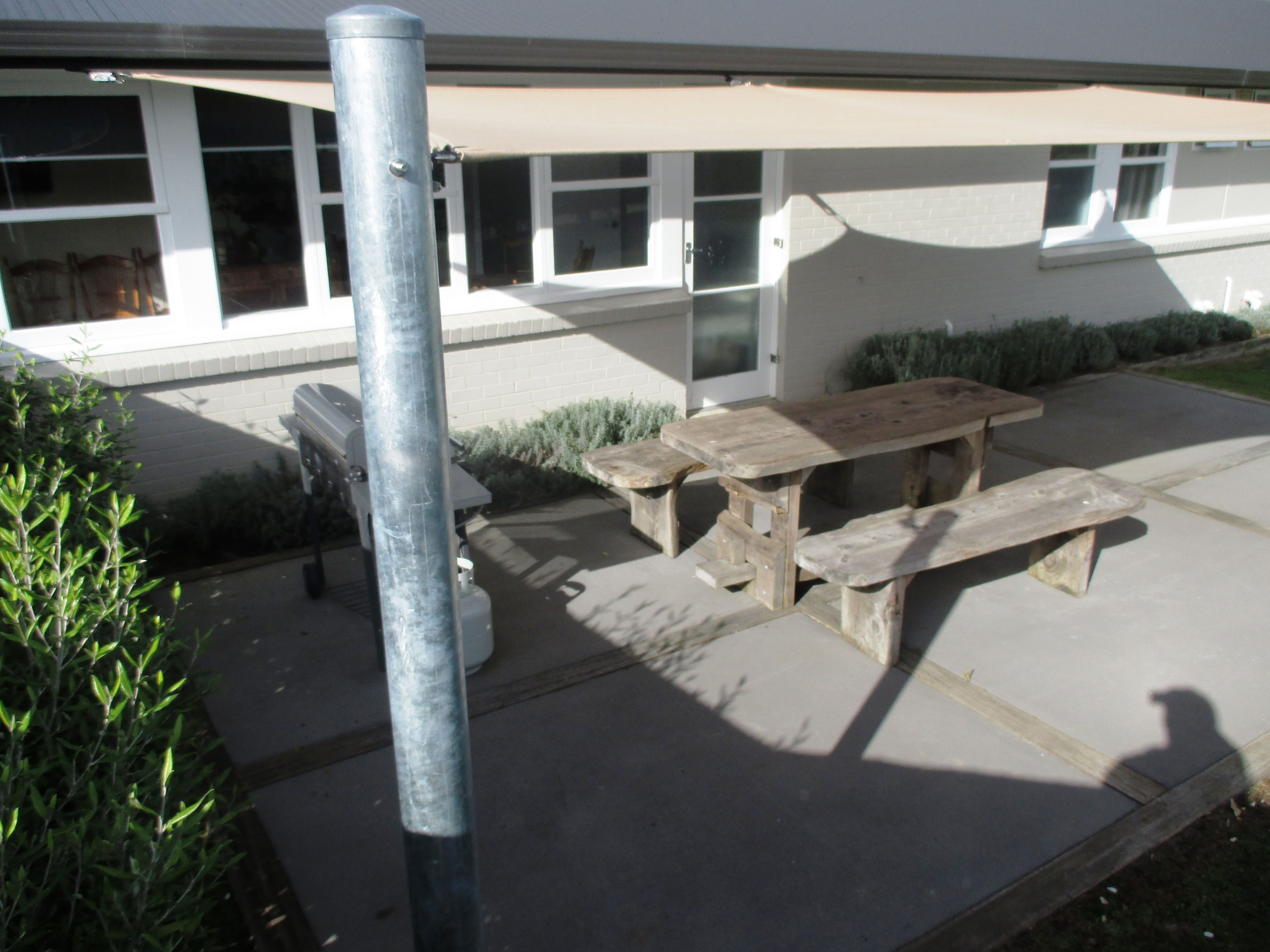 Un espace extérieur aménagé en terrasse, avec une table et des bancs en bois, un poteau en métal, et un bâtiment aux grandes fenêtres en arrière-plan.