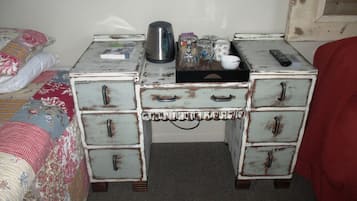 A small, rustic bedroom with a bed, a dresser with multiple drawers, and a nightstand with a kettle and other items.