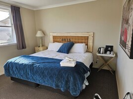 Cama bem arrumada com colcha azul, cabeceira de madeira com a palavra "OWLS" e mesa de cabeceira com luminária, além de uma bandeja com itens para café.