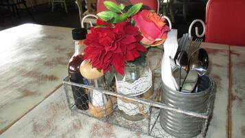 A table with a metal tray holding a bottle, a jar, a lace doily, and a metal cup with utensils.