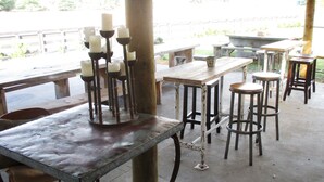 An outdoor seating area with wooden tables and stools, a candle holder, and a concrete floor. - Fat Owl Motel, Bar & Eatery (Piopio)