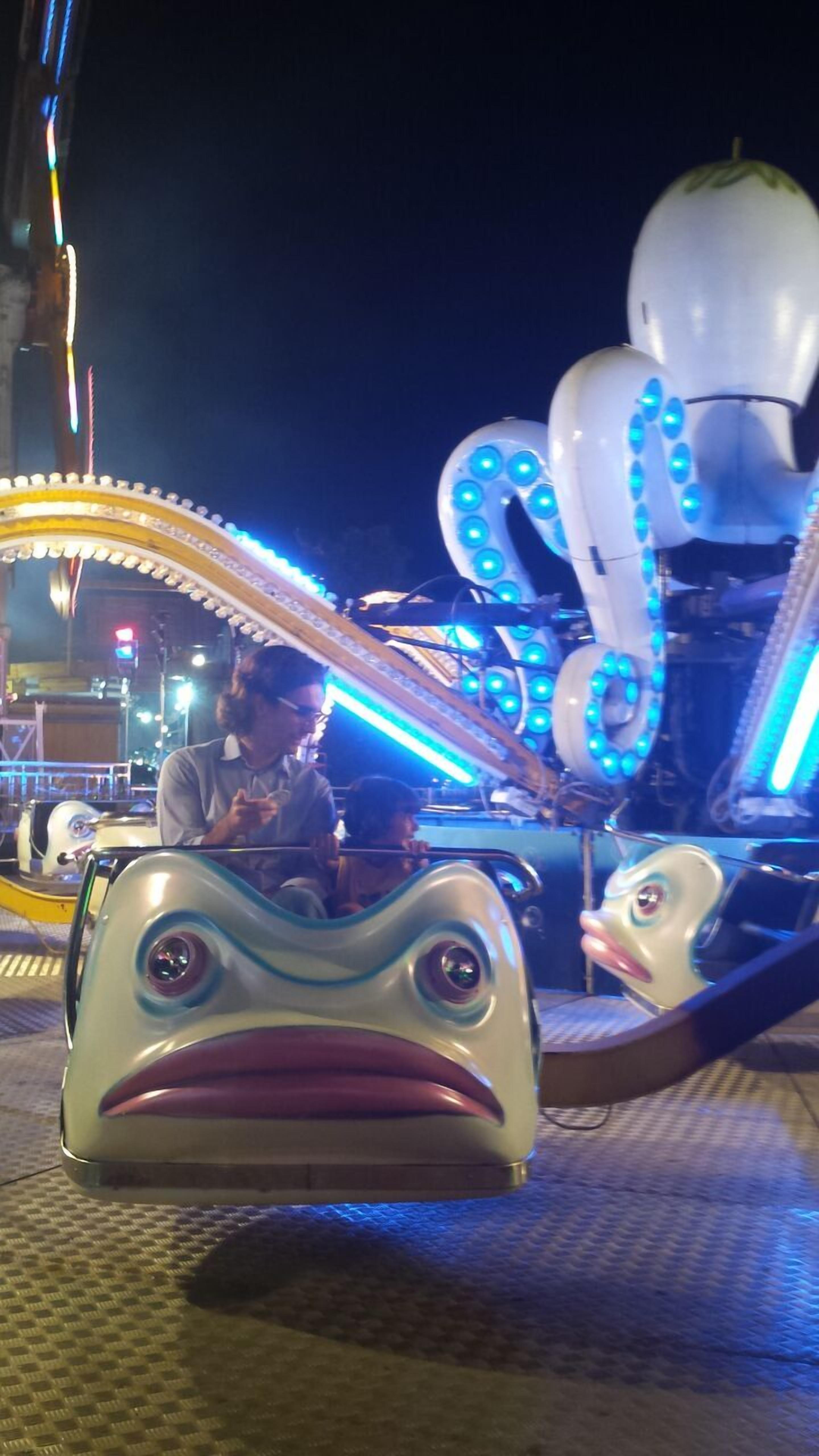 Una atracción de parque de diversiones con una gran estructura de pulpo iluminado y un vehículo con forma de rana.
