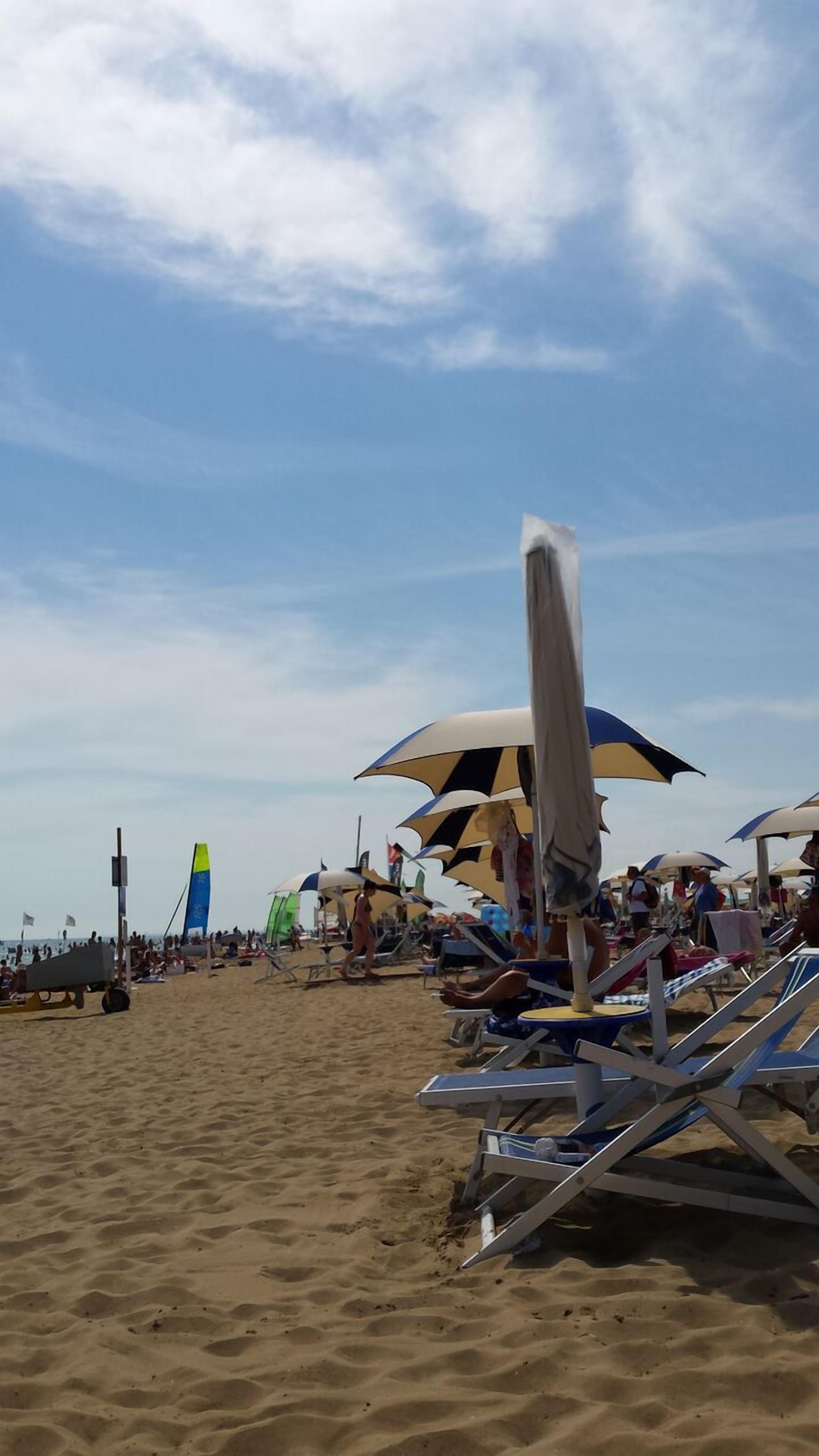 A beach with sun loungers and umbrellas, a lifeguard stand, and a large inflatable structure in the background.