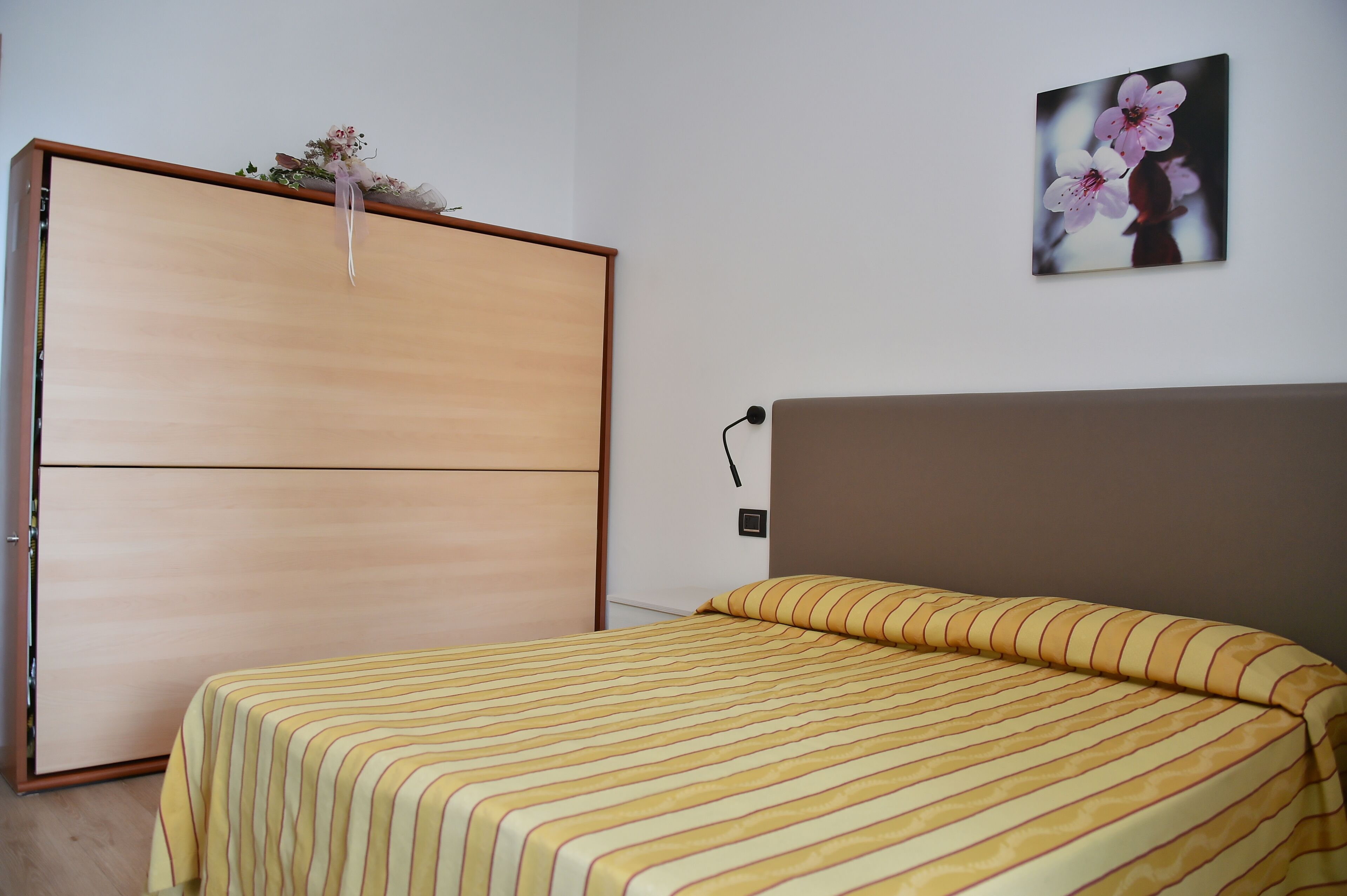 Un dormitorio con una cama, un armario de madera y un cuadro de flores colgado en la pared.