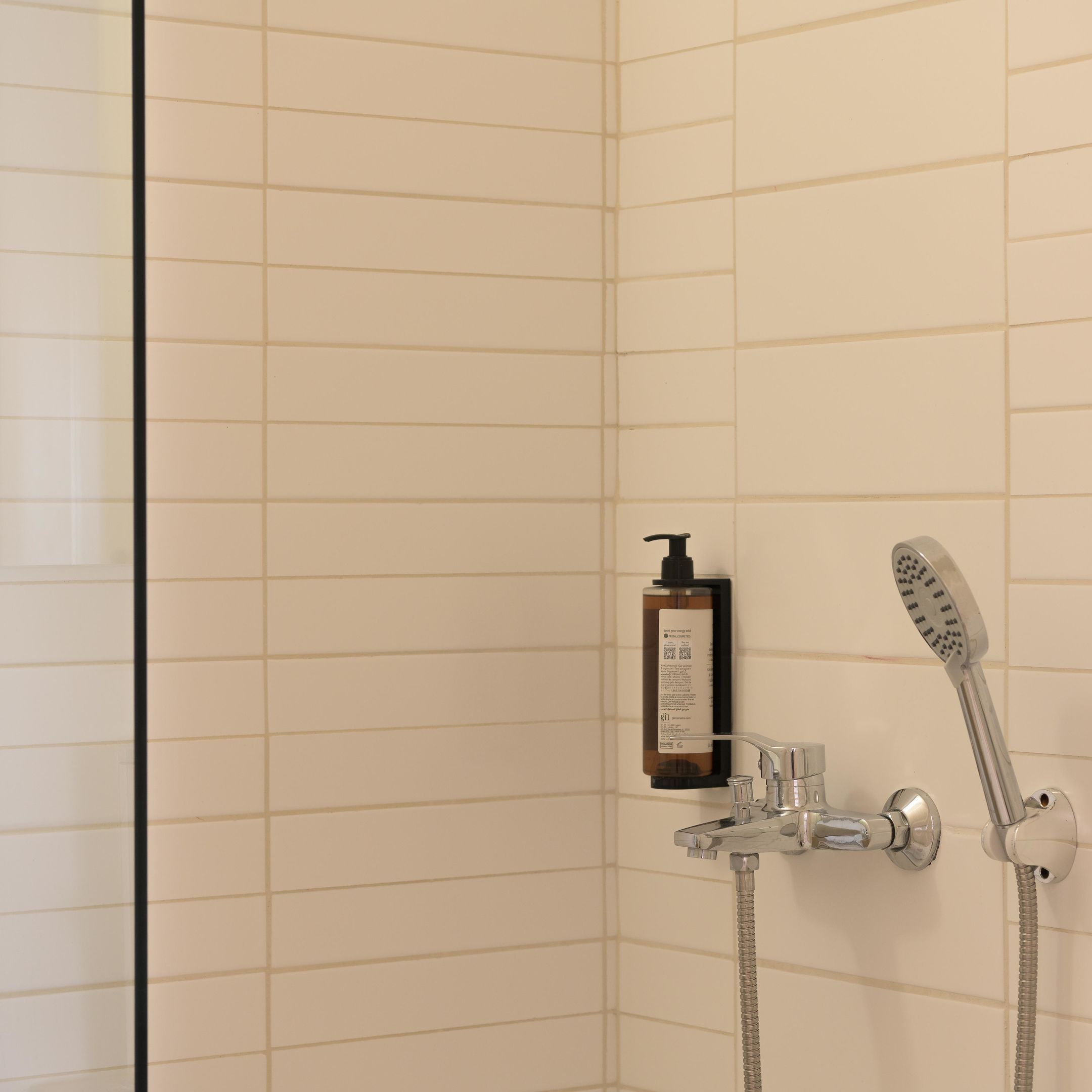 A shower with a handheld showerhead and a bottle of shampoo.