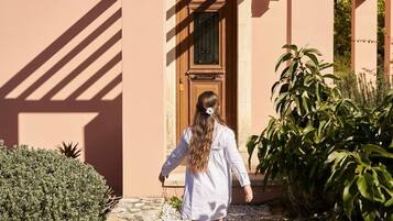 A woman walking towards a building with a tiled roof and a wooden door.