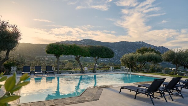 A swimming pool with lounge chairs, surrounded by trees and a mountainous backdrop.