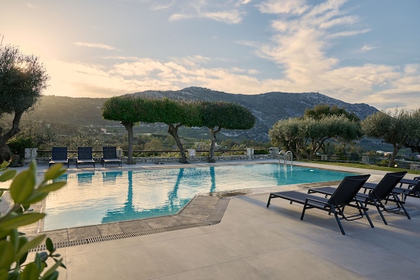 Ein Swimmingpool mit Liegestühlen, umgeben von Bäumen und einer Bergkulisse.