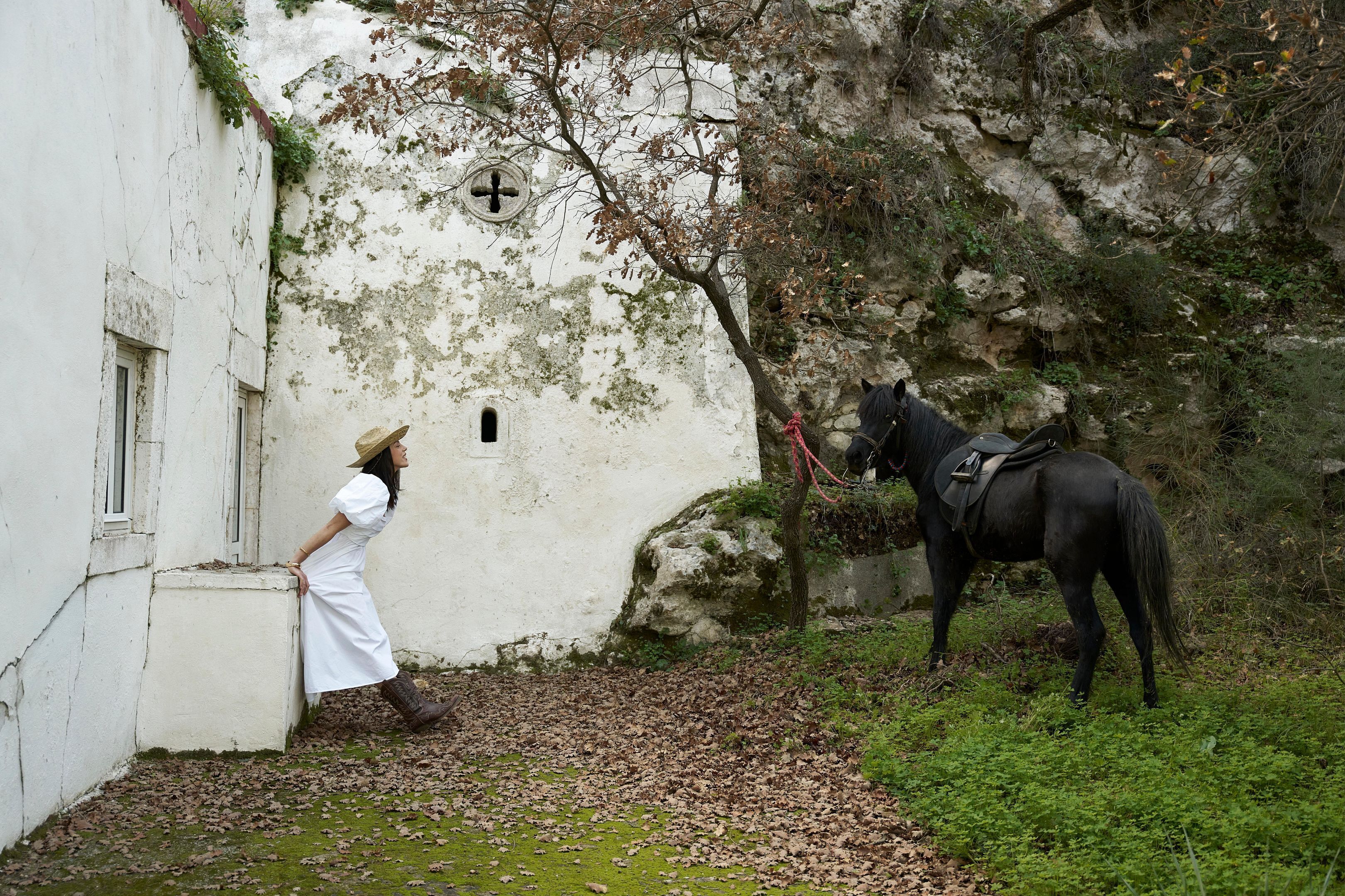 Un edificio blanco con un símbolo de cruz, un caballo y una persona apoyada en la pared.