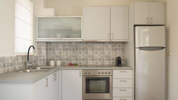 A modern kitchen with white cabinets, a stainless steel refrigerator, a built-in oven, and a tiled backsplash.