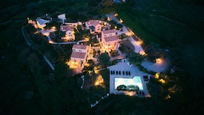 An aerial view of a residential area with multiple houses, a swimming pool, and well-lit pathways.