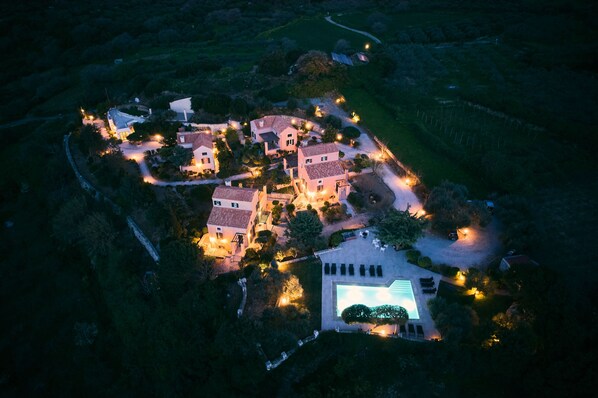 An aerial view of a residential area with multiple houses, a swimming pool, and well-lit pathways.