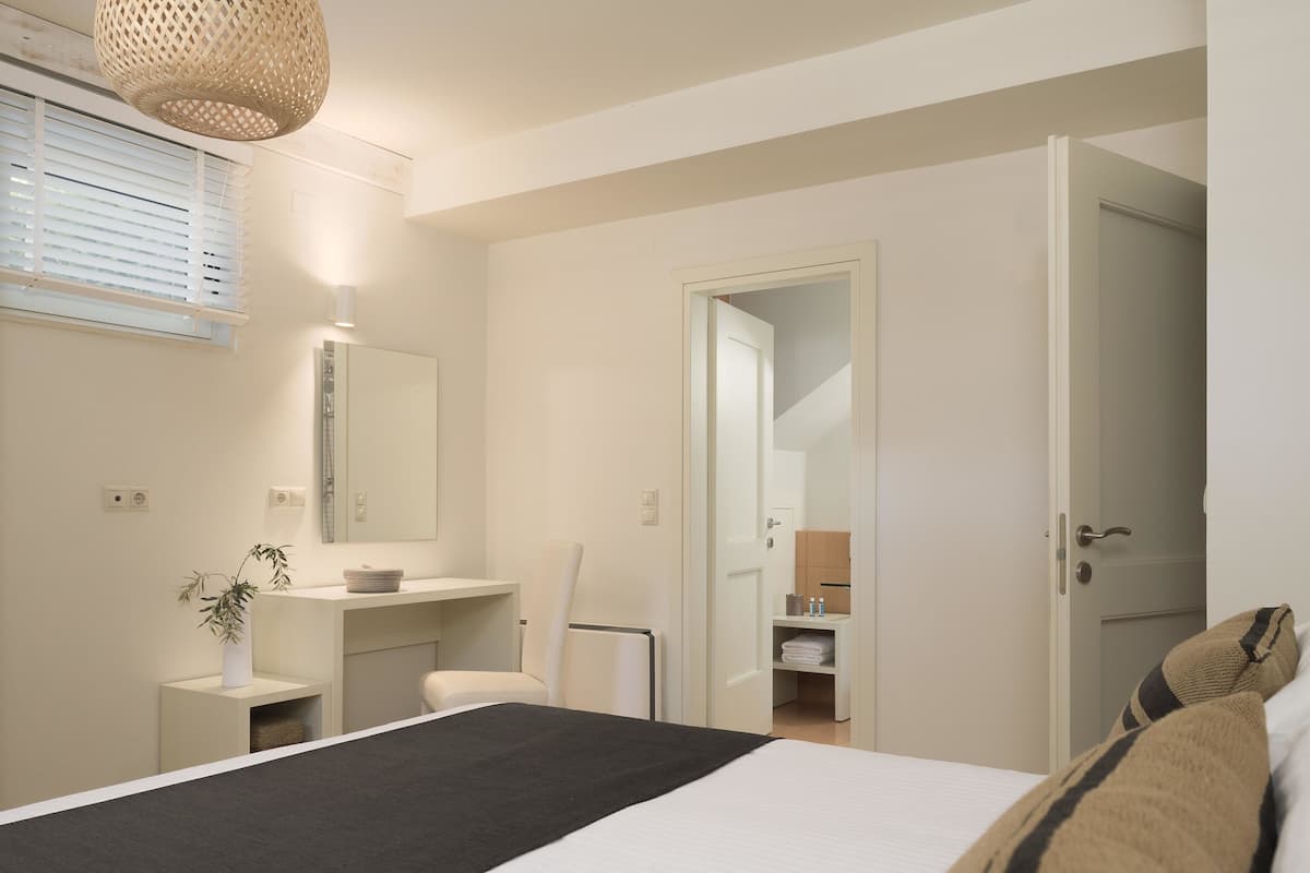 A bedroom with a bed, bedside table, chair, and a bathroom visible through an open door.