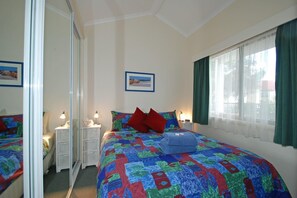 A bedroom with a large bed, a bedside table with a lamp, a mirror, and a window with curtains. - Triabunna Cabin and Caravan Park (Triabunna)