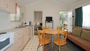 A compact kitchen with a dining area, a TV, and a sofa. - Triabunna Cabin and Caravan Park (Triabunna)
