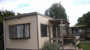A small, single-story mobile home with a beige exterior and a wooden deck. - Triabunna Cabin and Caravan Park (Triabunna)