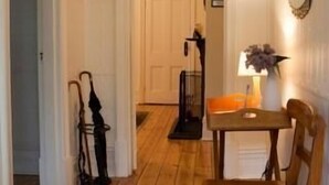 A hallway with wooden flooring, a red patterned rug, a wooden chair, a small table with a lamp, and a mirror on the wall. - Brown's House Bed and Breakfast (Boconnoc Park)