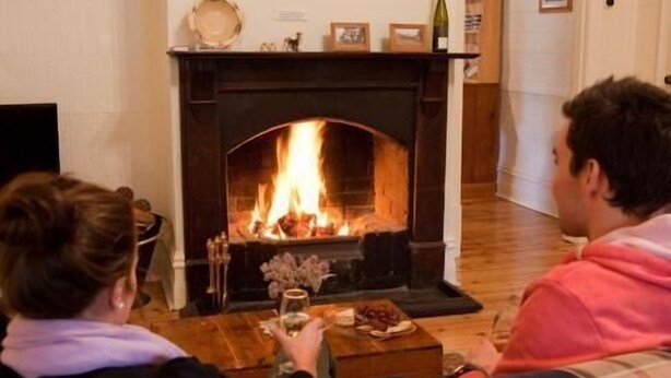 Two people sitting on a couch facing a fireplace with a fire burning. - Brown's House Bed and Breakfast (Boconnoc Park)
