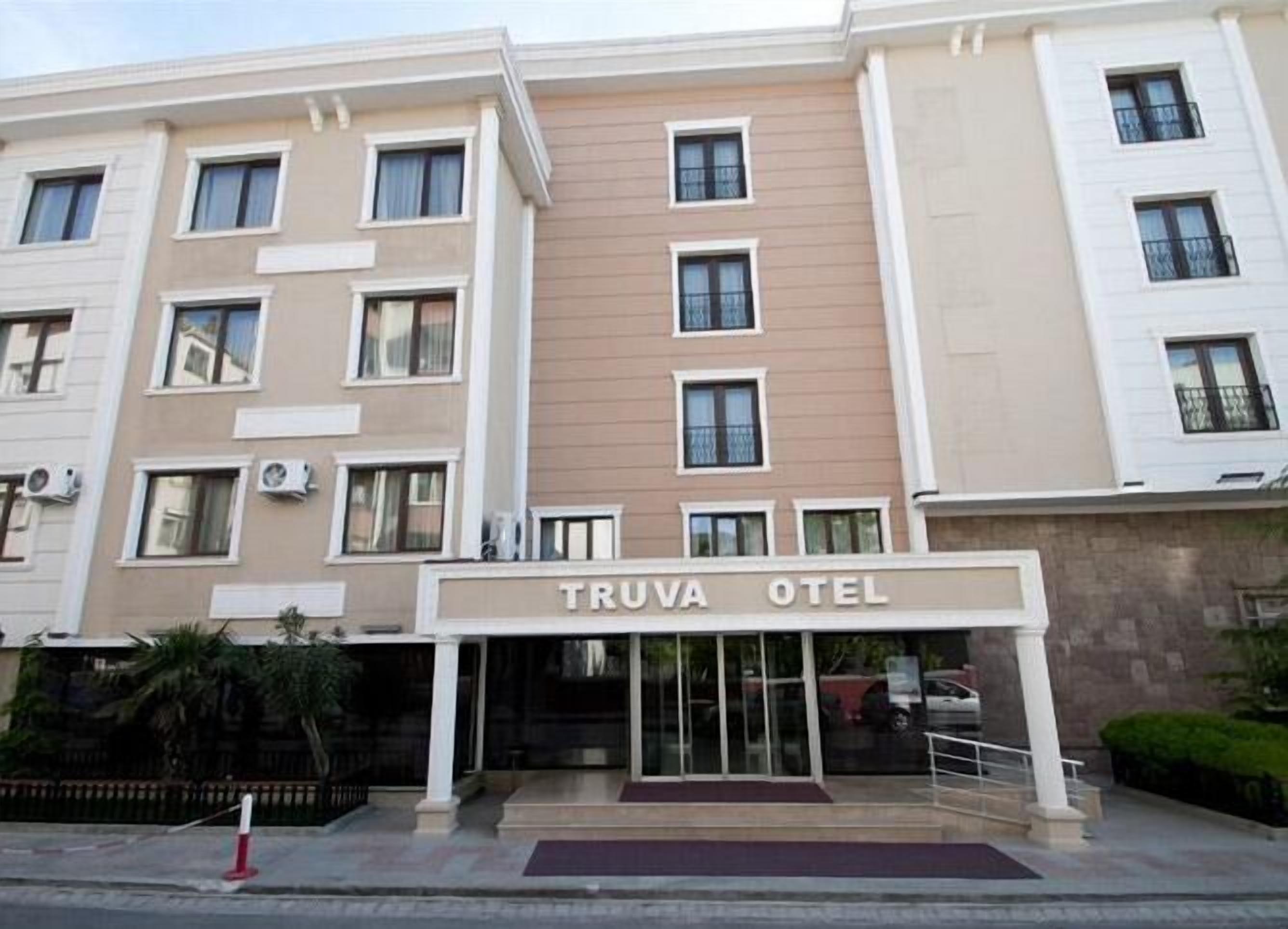 Un hôtel à plusieurs étages, doté d’une façade beige et blanche, d’une entrée centrale avec des portes vitrées et de climatiseurs fixés aux murs extérieurs.