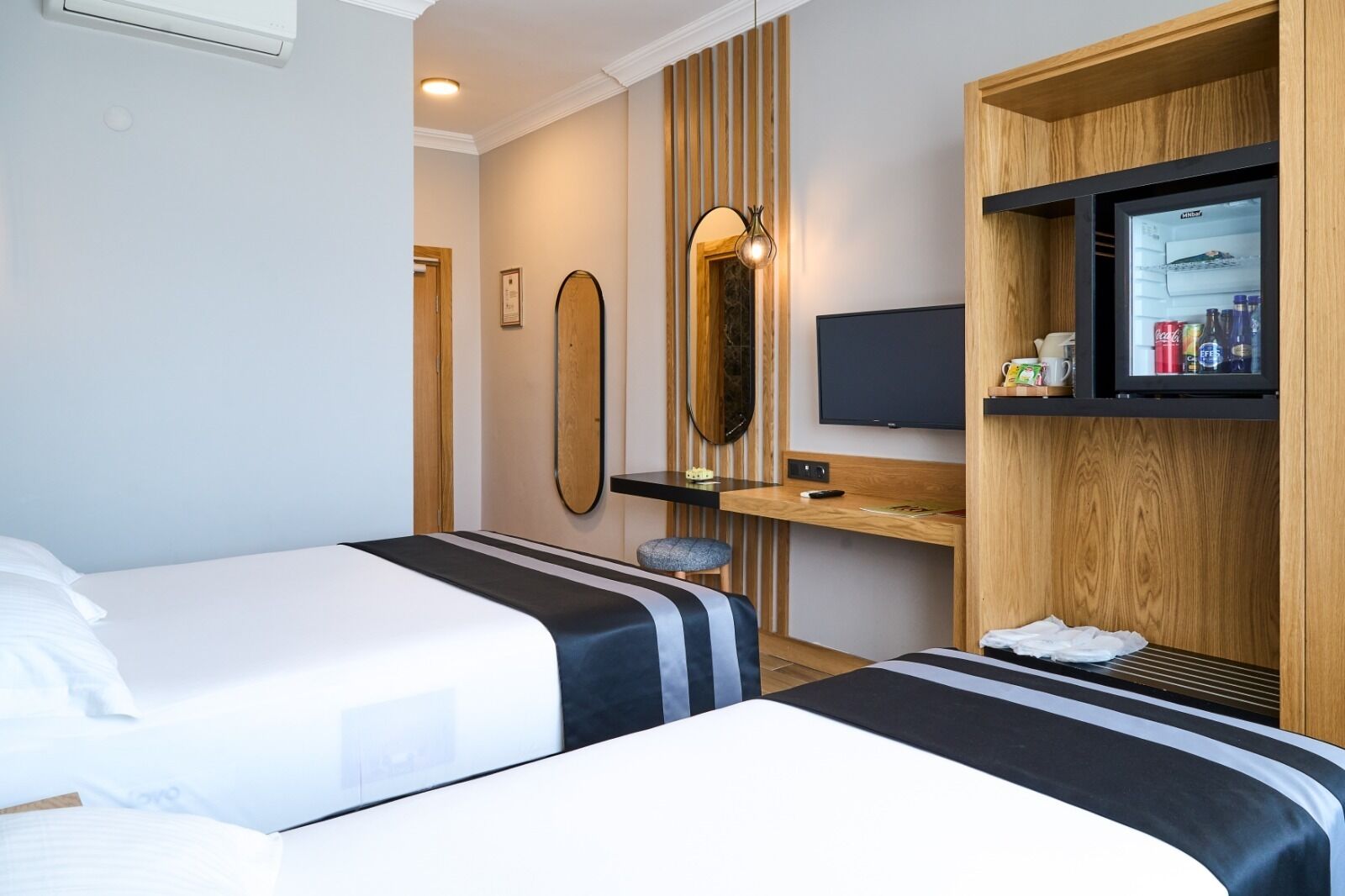 A hotel room with two beds, a desk, a TV, and a minibar.