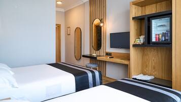 A hotel room with two beds, a desk, a TV, and a minibar.
