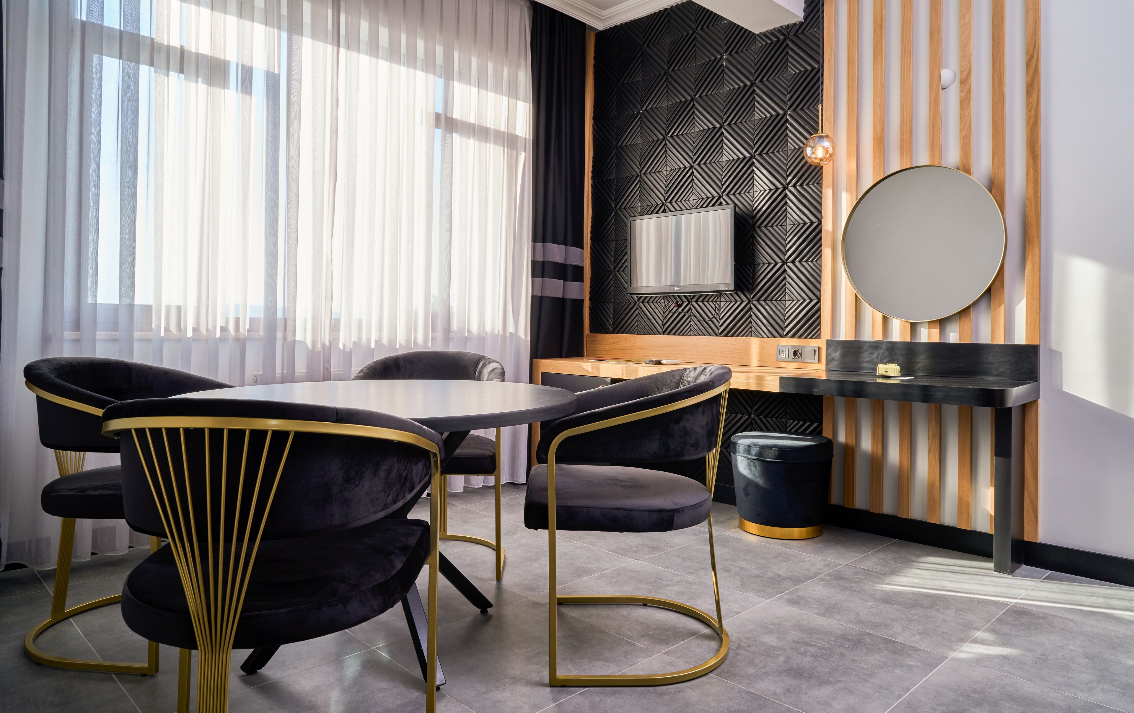A modern dining area with a round table, black velvet chairs with gold accents, a black and white striped wall, and a round mirror.