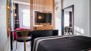 Habitació d'hotel moderna amb un llit gran, una televisió penjada a un panell de fusta, escriptori amb cadira i un mirall gran.