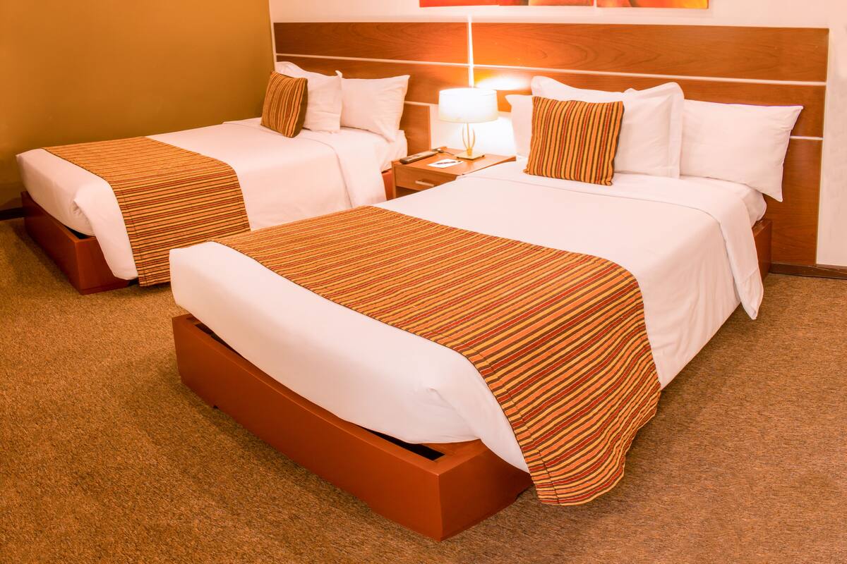 Une chambre d’hôtel avec deux lits, chacun recouvert d’une couvre-lit à rayures, doté d’une tête de lit en bois et agrémenté d’une table de chevet avec une lampe.