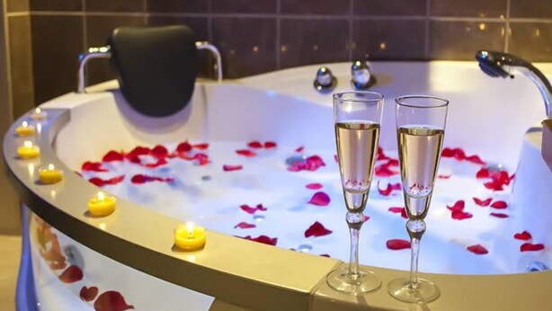Una bañera con pétalos de rosa y copas de champán.