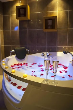 A bathtub with rose petals and champagne glasses.