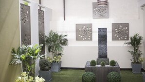 Un jardín interior moderno con césped artificial, plantas en macetas y decoración mural.