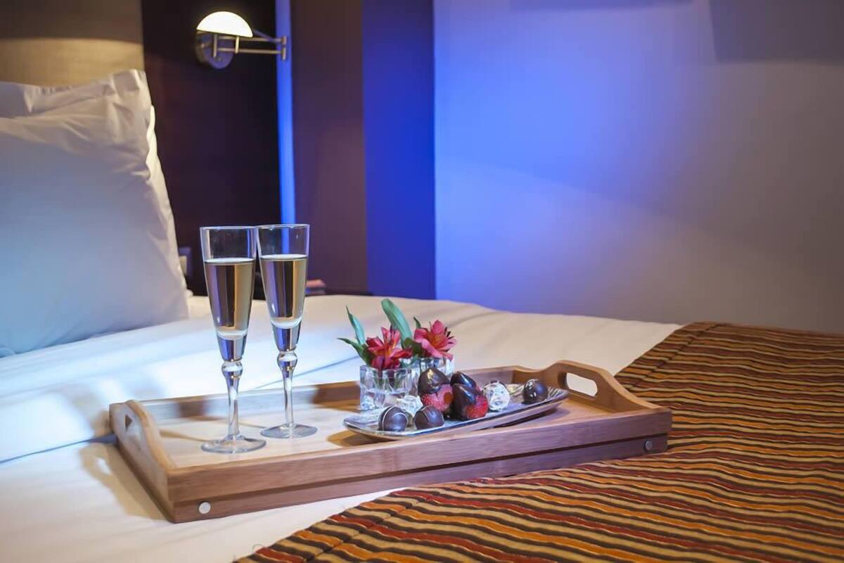 Un lit avec un plateau de chocolats, deux coupes de champagne, un oreiller et une lampe fixée au mur.