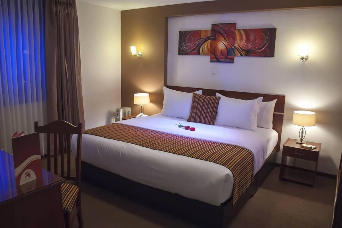Une chambre d’hôtel avec un grand lit, deux tables de chevet avec des lampes, une chaise et un tableau au mur.