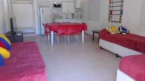 A living room with a red sofa, a dining table with red chairs, a kitchen area with white cabinets, and a colorful abstract art piece on the wall. - La Casa de Feli (Barreal)