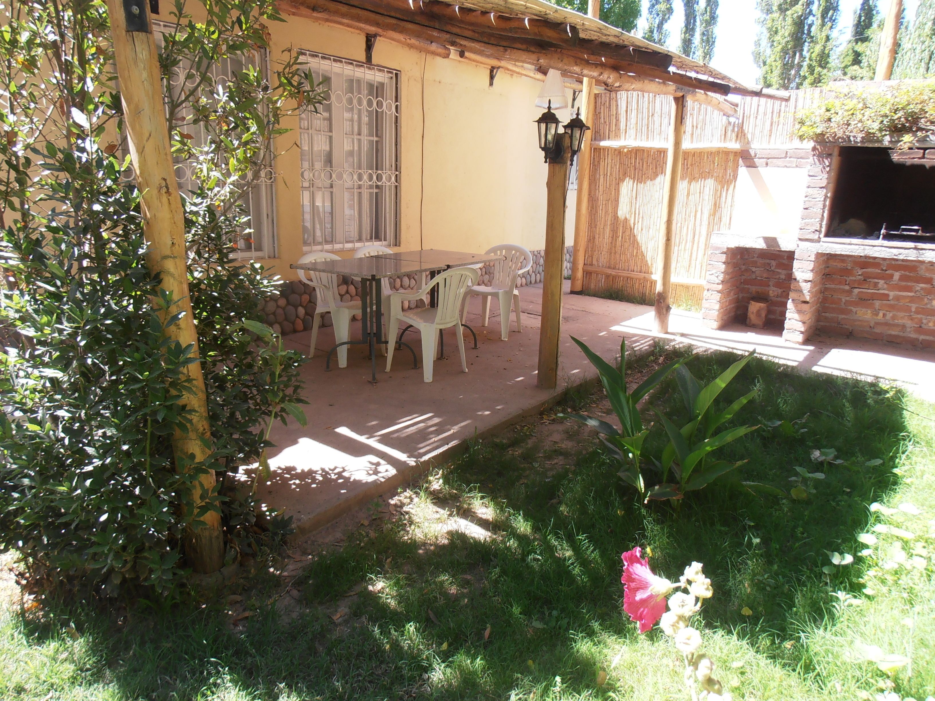 A patio with a table and chairs, a brick oven, and a garden with plants and a flower.