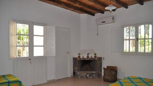 A room with a fireplace, two beds with colorful quilts, a wooden ceiling, and large windows. - La Casa de Feli (Barreal)