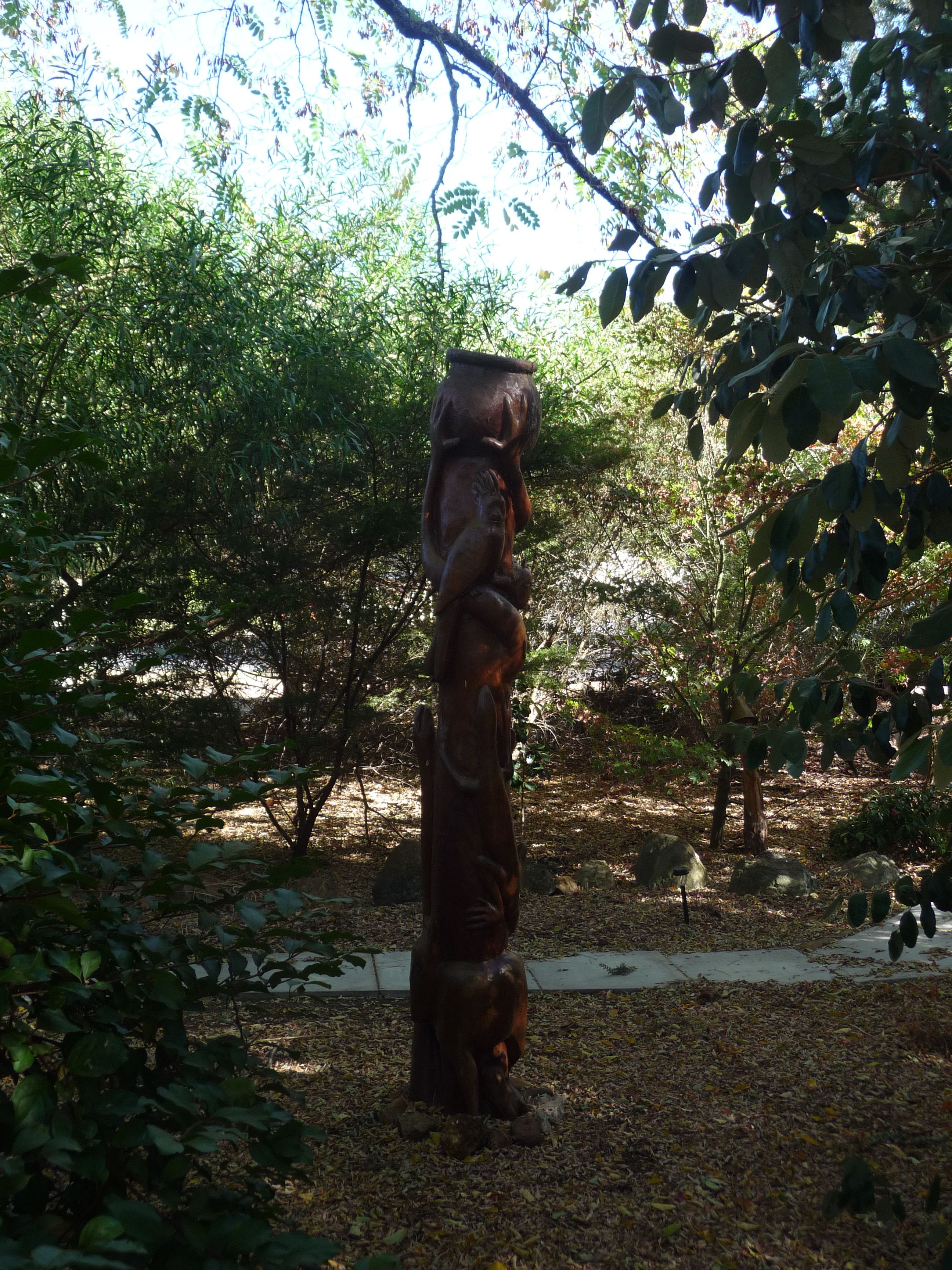 A sculpture of a figure in a forested area with trees and a path.