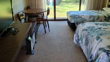Quarto de hotel com uma cama, uma escrivaninha com um computador e uma cadeira, uma mesa e vista para o exterior.