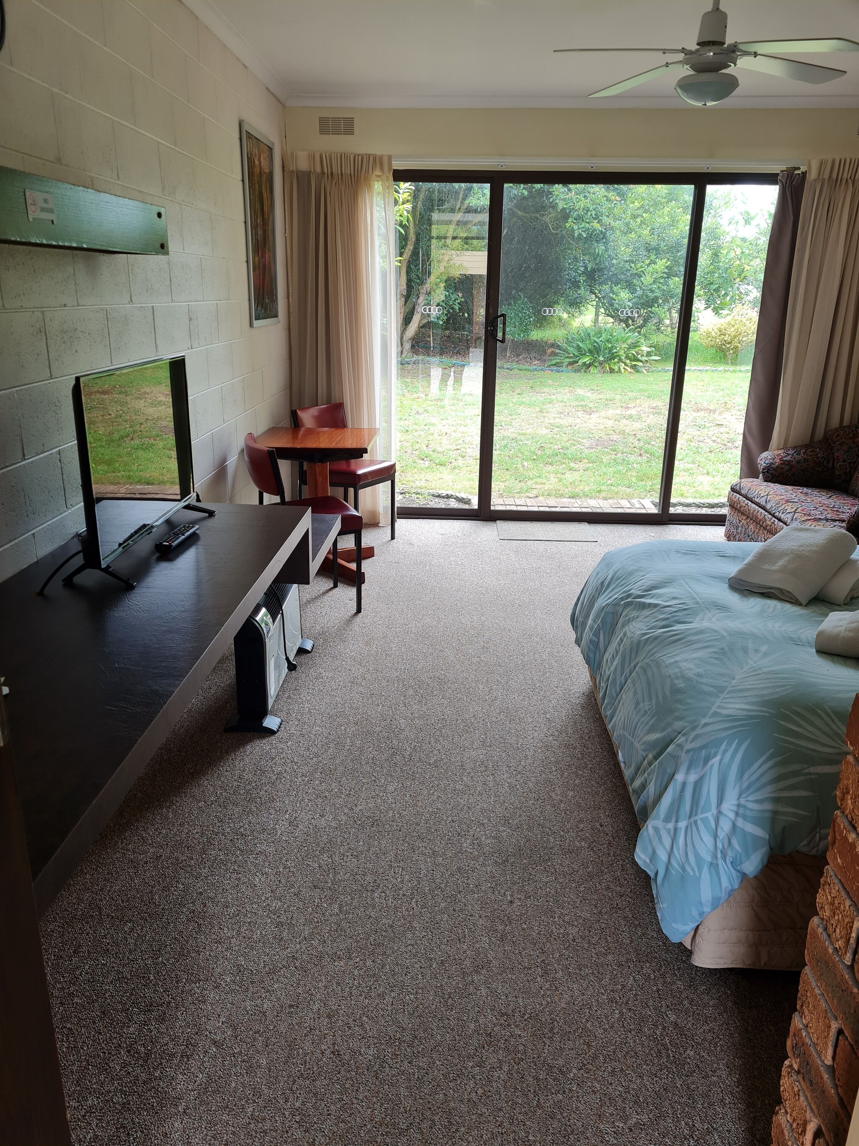Una habitación con una cama, un escritorio con una computadora, una silla y vistas al exterior por una puerta corredera.